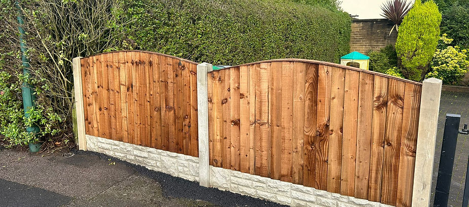 Wooden fence gate on a stone wall in front of a house with green shrubbery